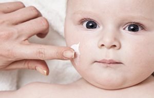 Une main d'adulte applique de la crème sur le visage d'un enfant.