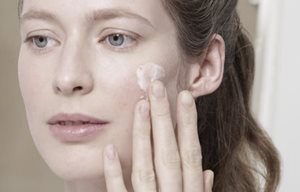 Femme qui s'applique de la crème sur la joue gauche.